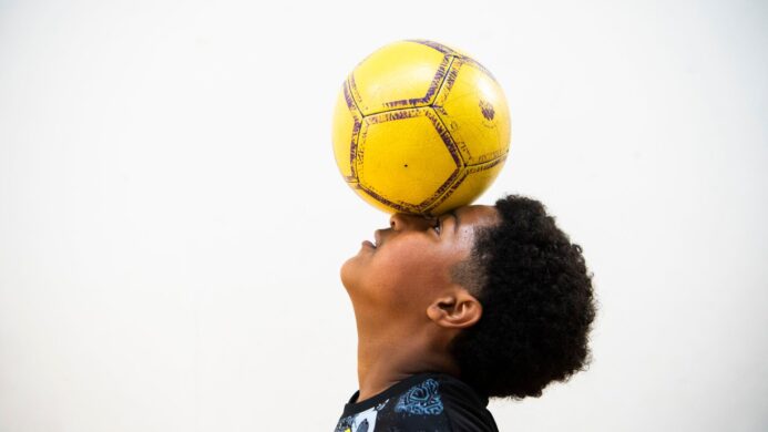 A young man balancing a yellow football on his head.