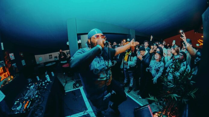 A man on stage with a mic in his hand, performing to a crowd at EartH